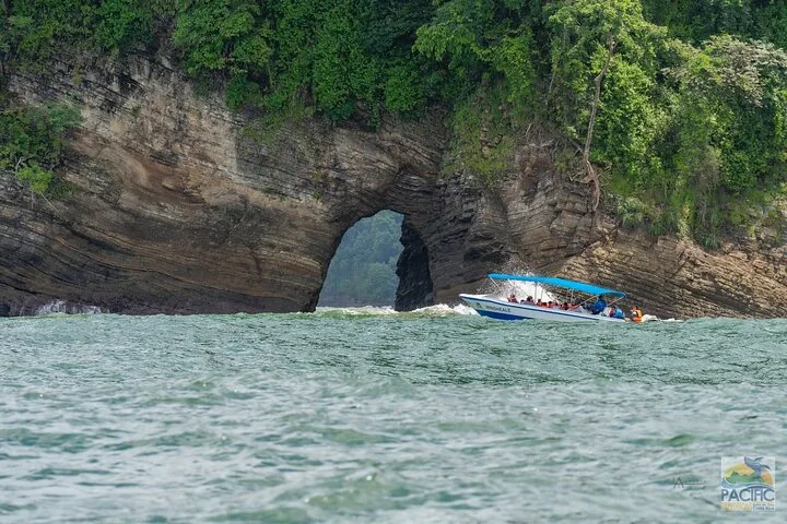 A tour boat traveling past a rocky cliff with a natural archway.