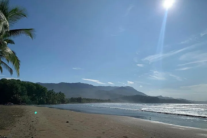 A wide sandy beach meeting the ocean under a bright, sunny sky.